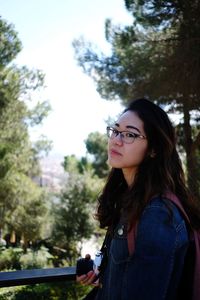 Portrait of young woman looking away while standing by trees