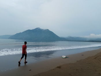 Rear view of man standing on beach against sky