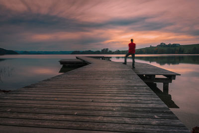 Man standing on pier over lake against sky during sunset