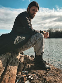 Young man sitting on shore against sky