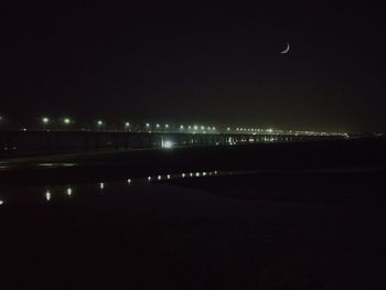 Illuminated city by river against sky at night