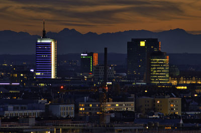 Illuminated buildings in city against sky at sunset
