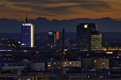 Illuminated buildings in city against sky at sunset