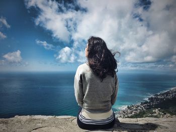 Rear view of woman looking at sea while sitting against sky