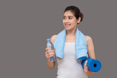 Portrait of smiling young woman holding bottle against black background