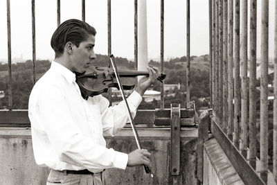 Side view of man playing violin while standing by railing