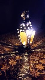 Close-up of illuminated lamp on table against wall