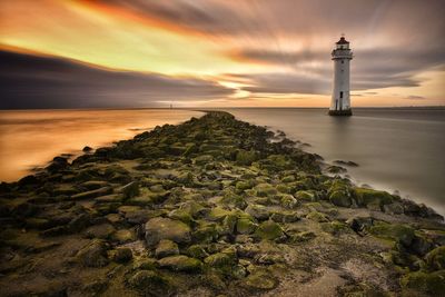 Lighthouse by sea against sky during sunset