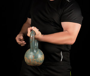 Midsection of man lifting kettlebell against black background