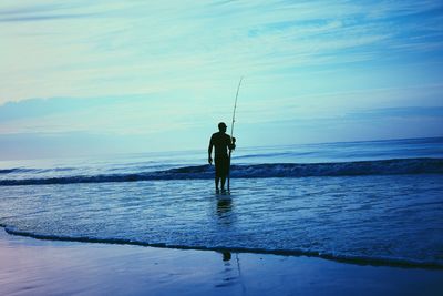 Rear view of man fishing in sea against sky