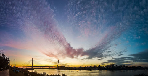 View of suspension bridge over river against cloudy sky