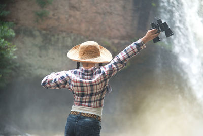 Rear view of woman holding binoculars against waterfall