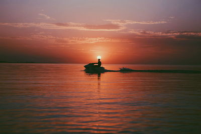Silhouette person jet boating in sea against sky during sunset
