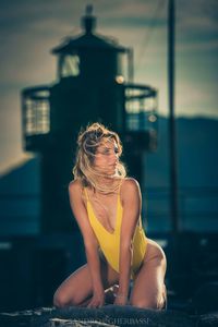 Woman in bodysuit kneeling against lighthouse