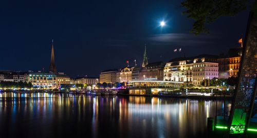 Illuminated cityscape reflecting on calm river against sky at night