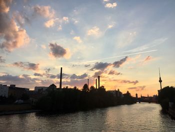 City by river against sky during sunset