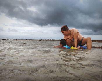 Side view of cute little child playing in sea against sky with his mother