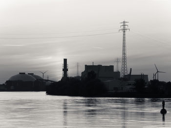 Silhouette electricity pylon by river against sky