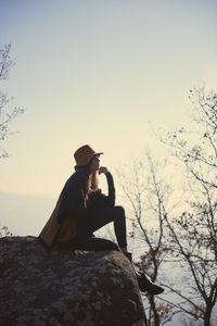 Side view of thoughtful woman sitting on cliff against sky