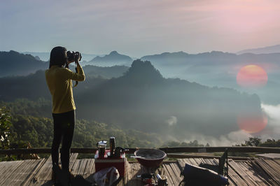 Rear view of woman photographing on mountain against sky