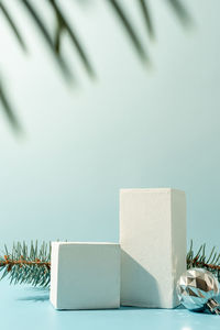 A minimalistic scene of podiums with christmas decorative balls and pine tree on a light blue