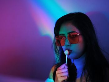 Young woman eating lollipop while looking away in illuminated room