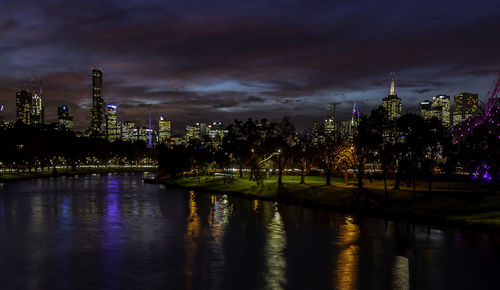 Illuminated buildings by river against sky at night