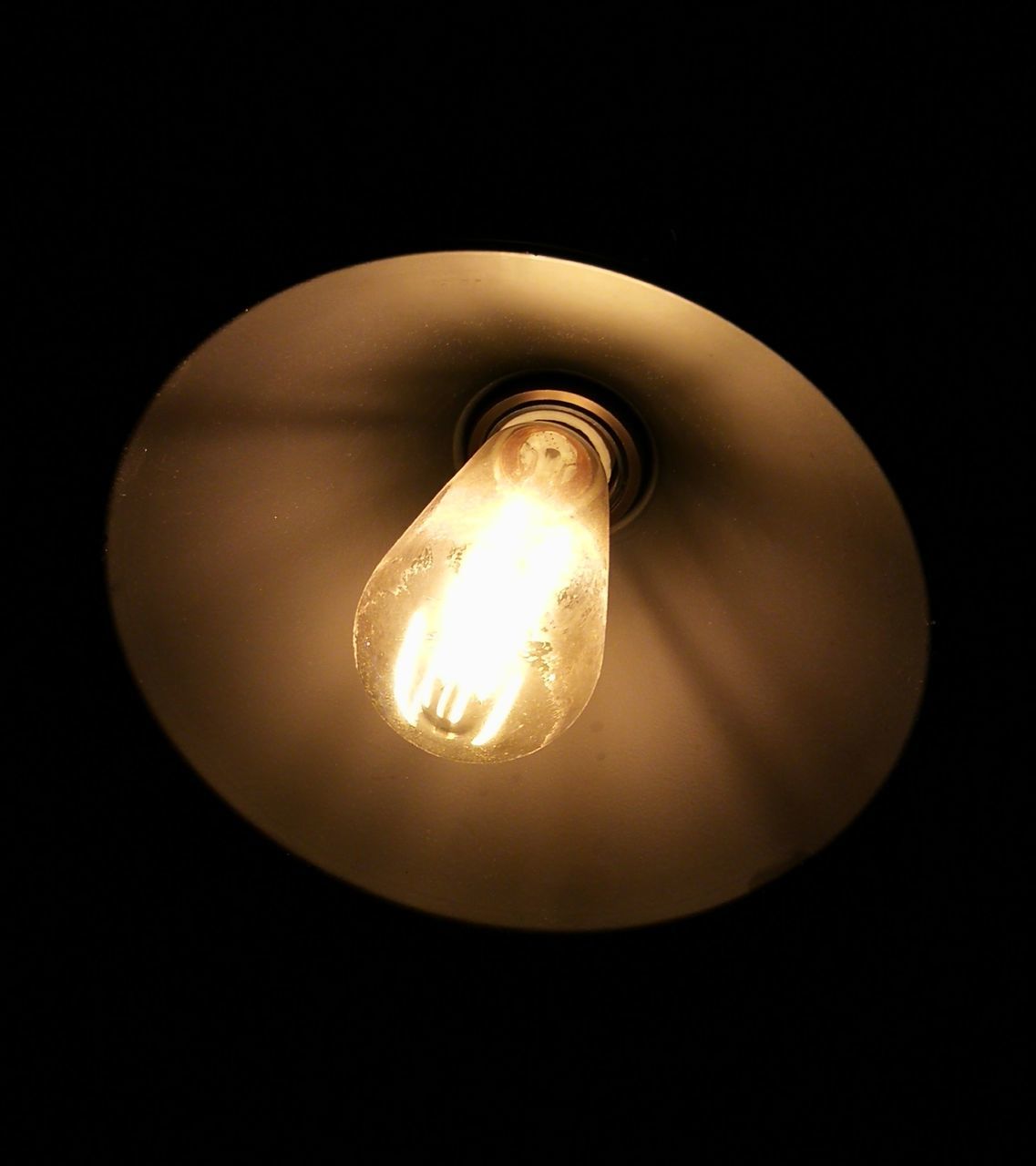 LOW ANGLE VIEW OF ILLUMINATED LIGHT BULB IN DARK ROOM