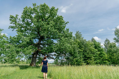 Rear view of woman standing in front of oak tree in a meadow