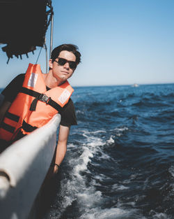 Portrait of man wearing sunglasses and life jacket on boat in sea