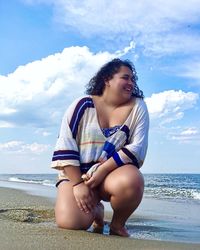 Happy young woman sitting on beach against sky