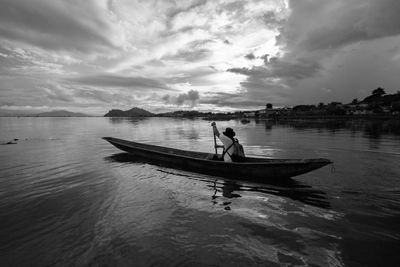 Rear view of man rowing boat in sea against cloudy sky