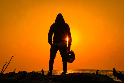 Silhouette man standing on beach against orange sky