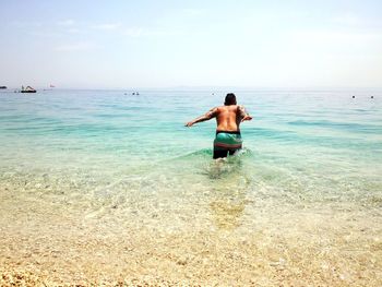 Rear view of shirtless man diving in sea against sky