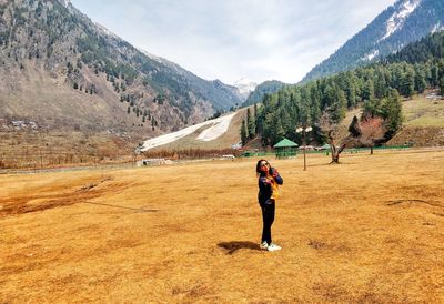 Full length of woman gesturing peace sign while standing on land against mountains