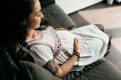 Pregnant woman touching belly while sitting at home