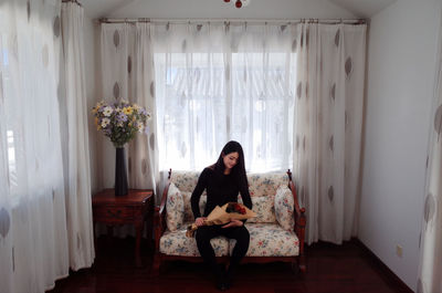 Woman sitting with flower bouquet against window at home