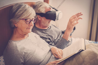 Senior woman reading book while man using virtual reality at home