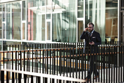 Full length of businessman using smart phone while walking in atrium