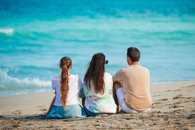 Rear view of woman sitting at beach against sky