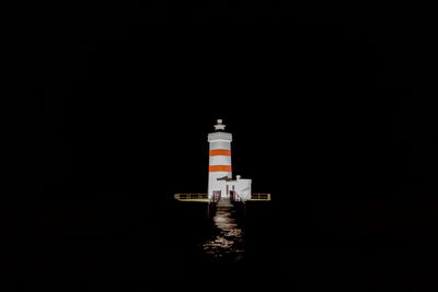 Lighthouse by sea against clear sky at night