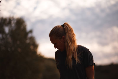 Woman looking away while standing against sky during sunset