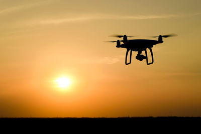 Low angle view of silhouette drone flying against orange sky