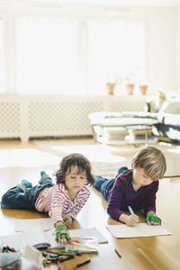 Friends coloring in books while lying on floor at home