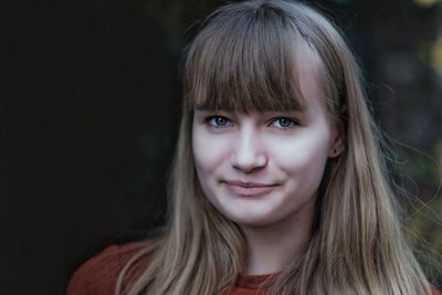 Close-up portrait of teenage girl with blond hair standing outdoors