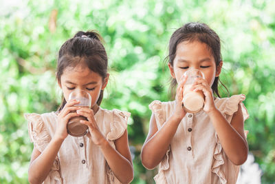 Friends drinking milk from glasses against trees