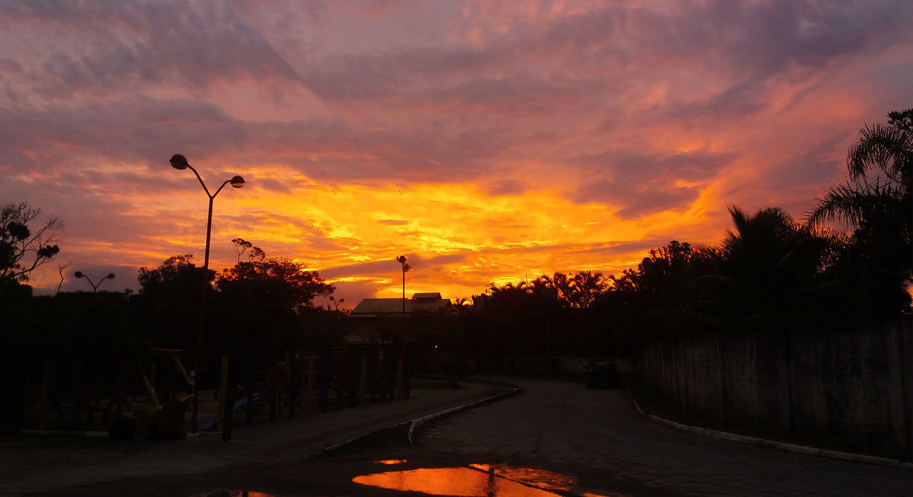 STREET AMIDST SILHOUETTE TREES AGAINST DRAMATIC SKY