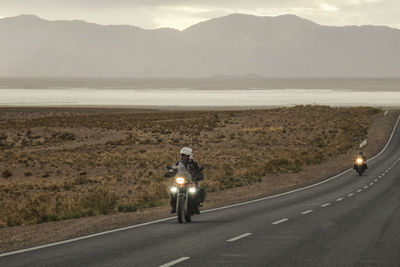 Man riding motorcycle on road against mountains