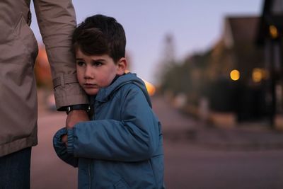 Sad boy looking away while holding hands with father during autumn