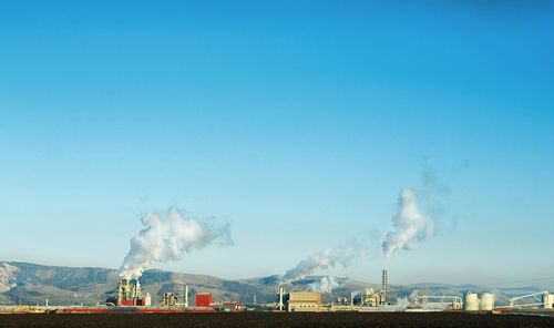 Smoke emitting from chimney at industry against blue sky